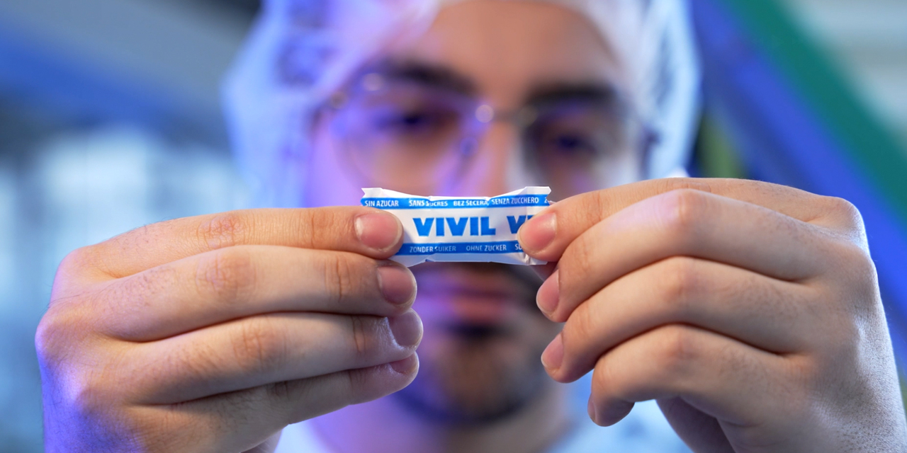 Startseite_Über uns banner Ein blaues VIVIL-Bonbon wird von einer Person in die Kamera gehalten